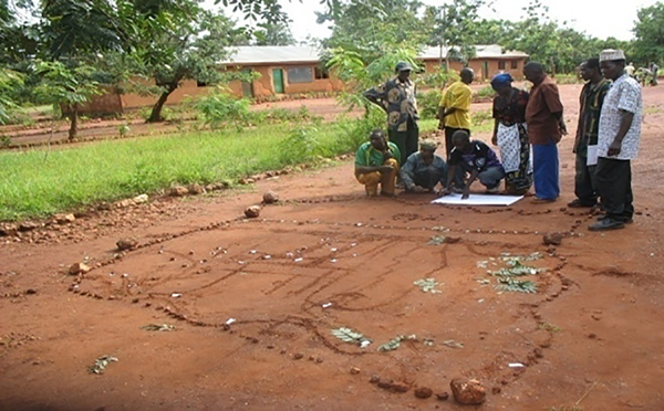 A group of men and women in a village in Tanzania look over a map of their community drawn and paper and in the dirt in front of them.